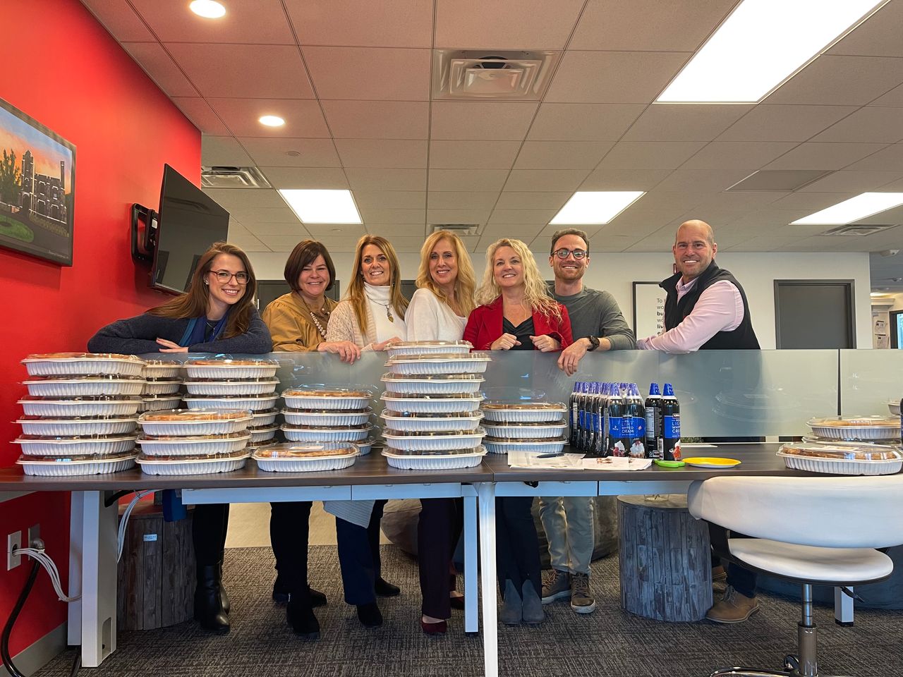 The team standing behind a table stacked with Thanksgiving pies at the office