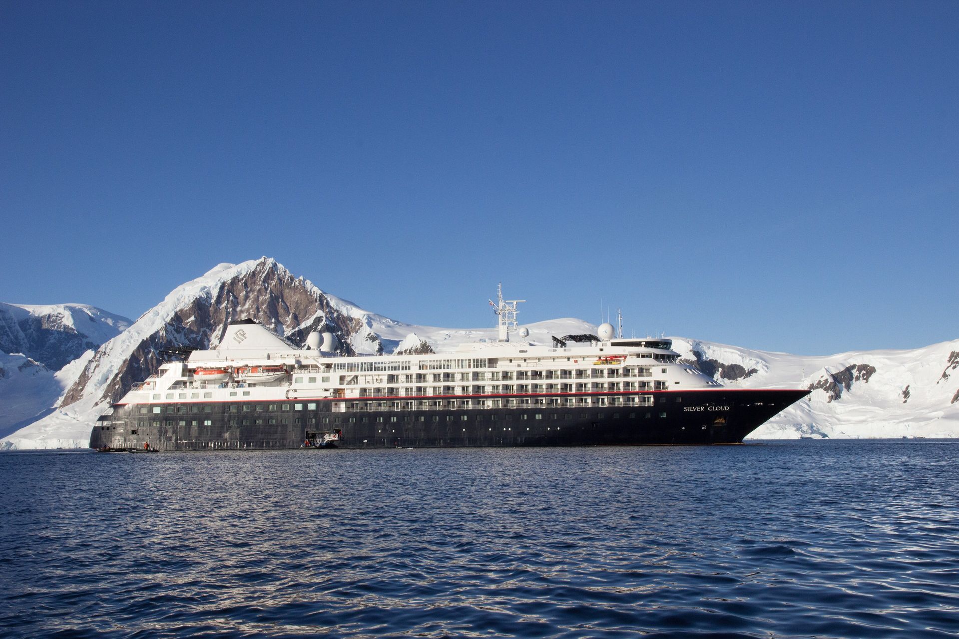 Silversea's Silver Cloud, a white ship with a dark hull, at anchor below snow-covered mountains in Paradise Bay, Antarctica