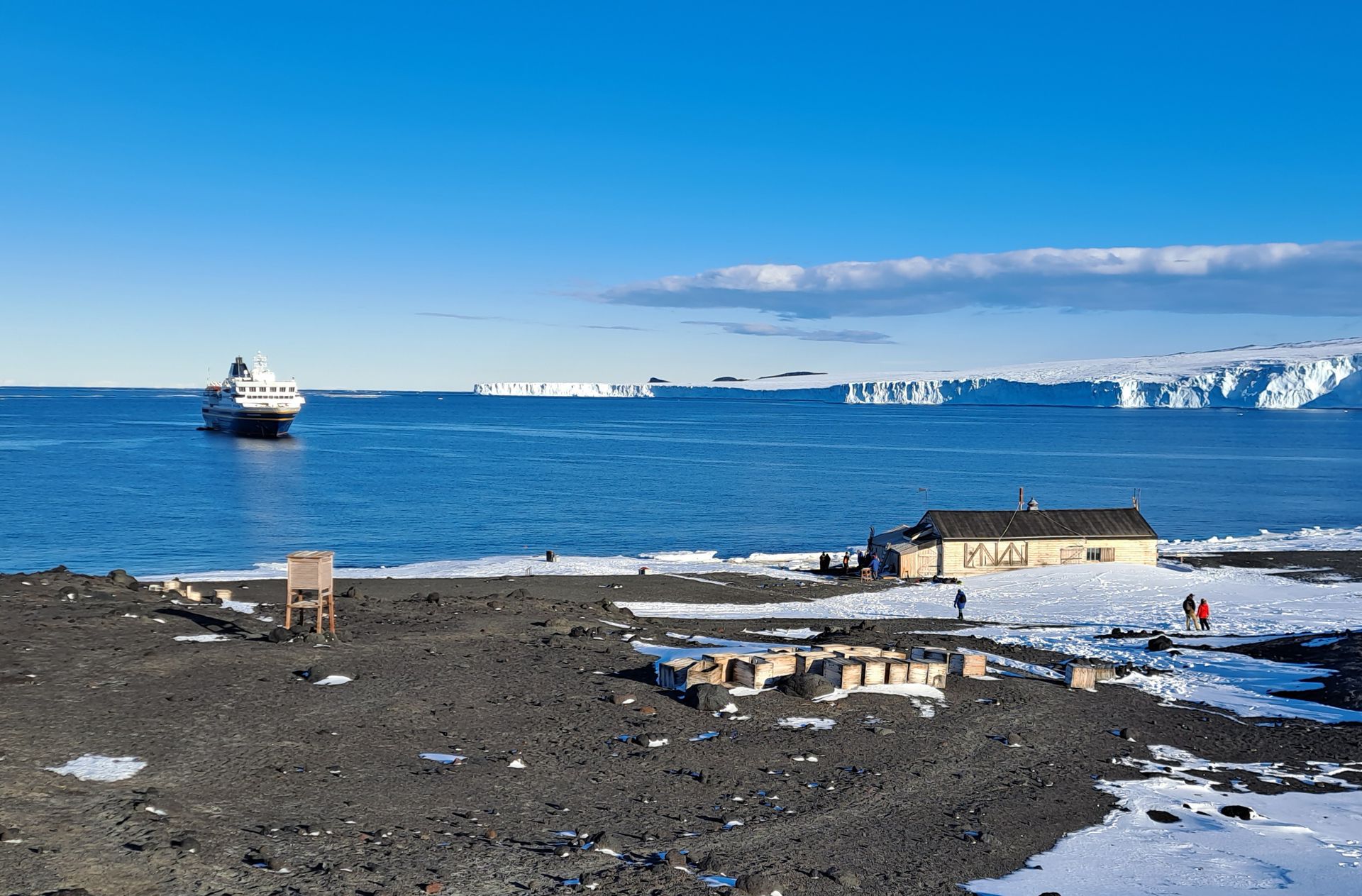 Scott's wooden hut at Cape Evans on Ross Island, with Heritage Adventurer at anchor and ice cliffs beyond
