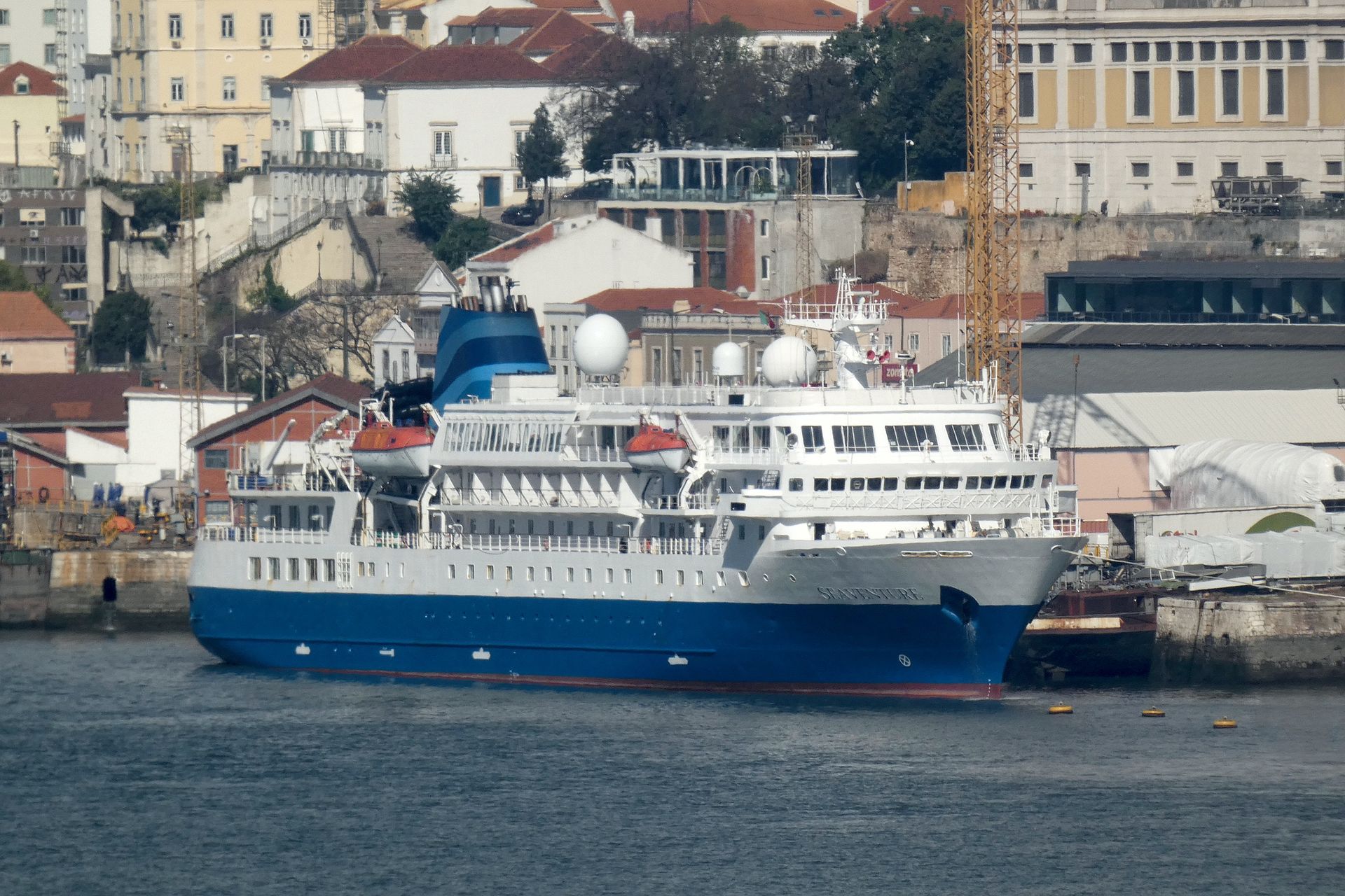 Seaventure, with a blue hull and white superstructure in its earlier livery, moored at a shipyard quay in Lisbon, Portugal, in April 2023