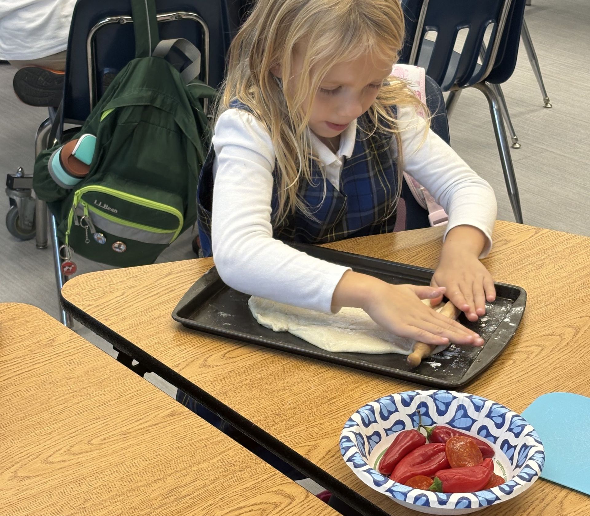 A girl decorating her treat on a baking tray beside a bowl of strawberries