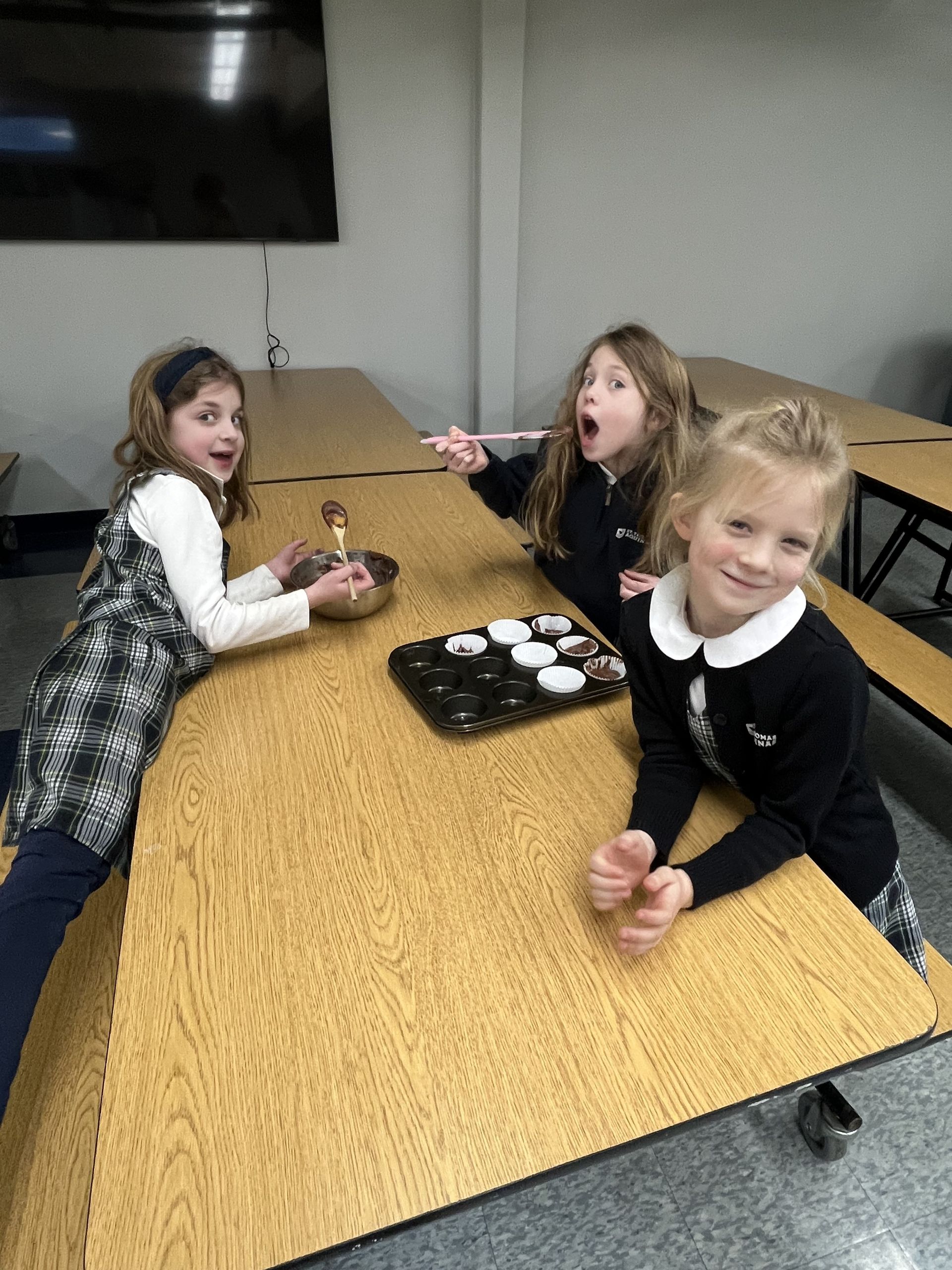 Three smiling girls sharing chocolate batter and a muffin tin