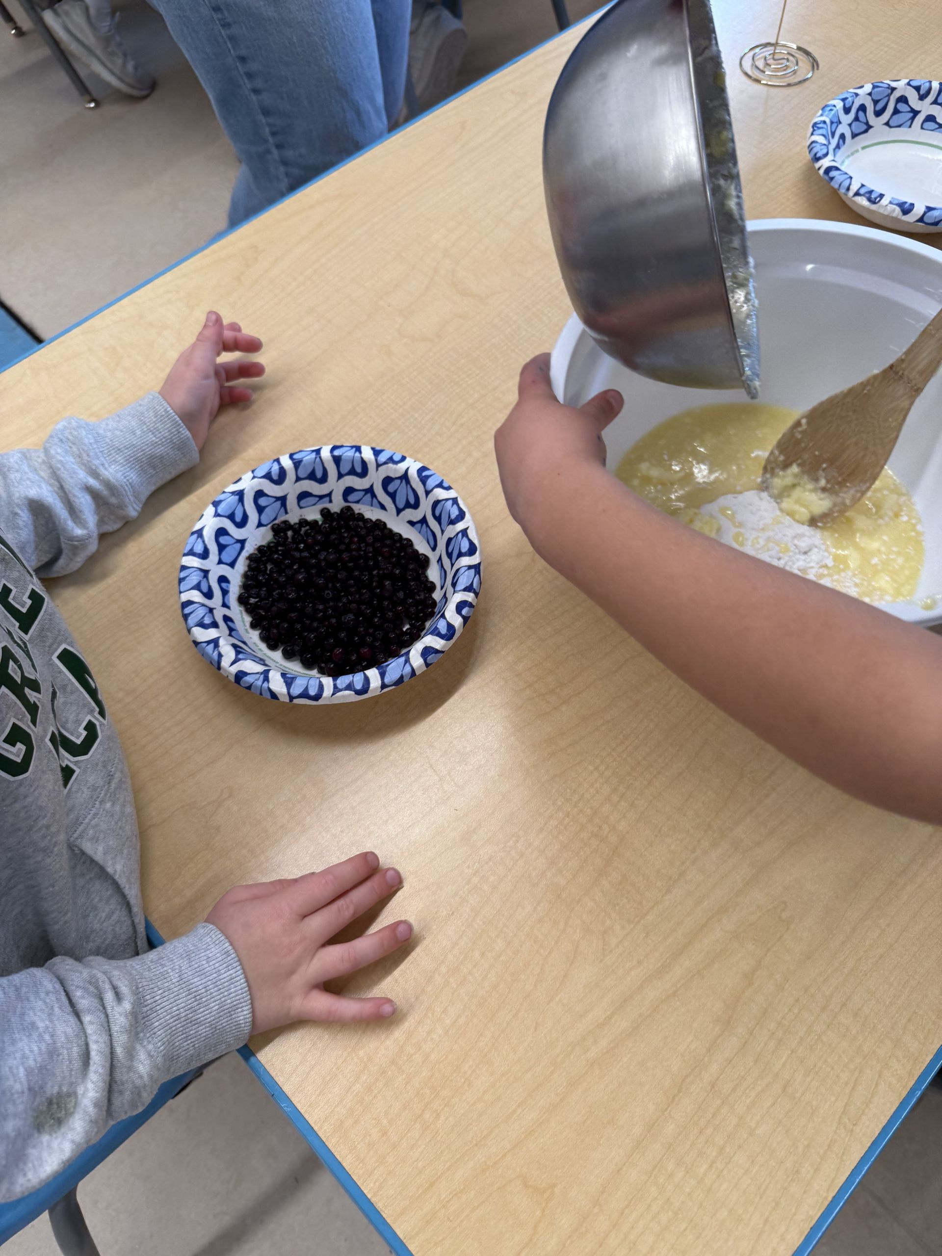 A child pouring batter beside a bowl of blueberries