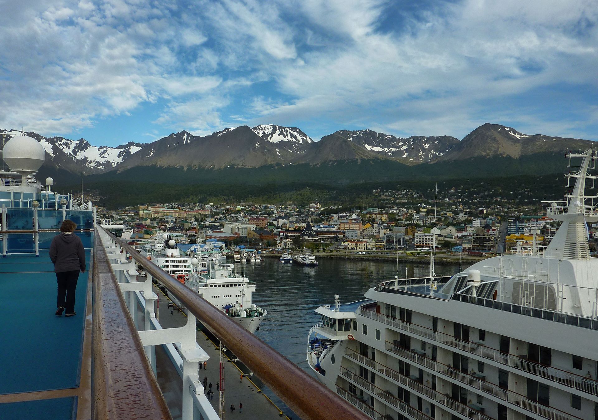 Ships moored at the pier in Ushuaia, Argentina, below snow-streaked mountains, seen from the upper deck of a cruise ship