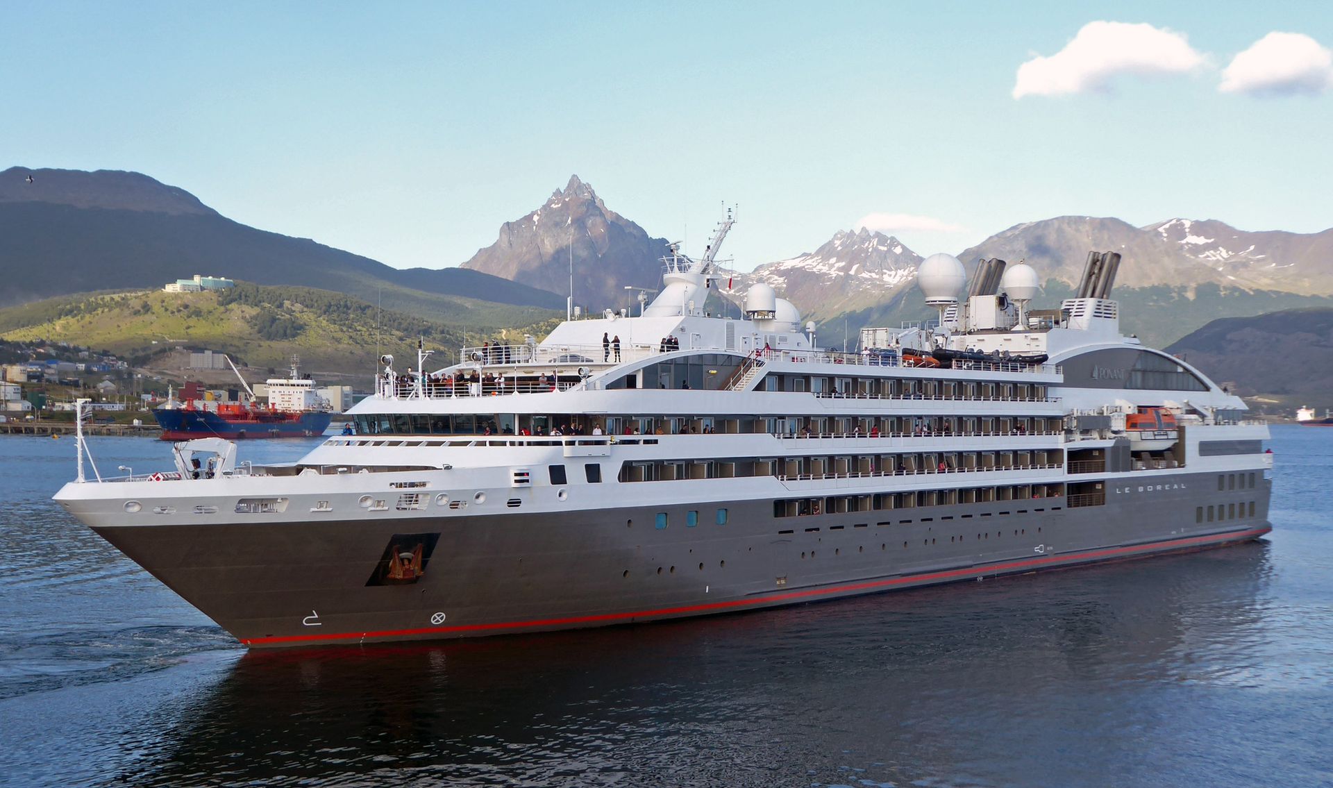 Ponant's Le Boréal, white with a gray hull and its name near the stern, underway in the harbor at Ushuaia, Argentina, with snow-streaked mountains behind, December 2019