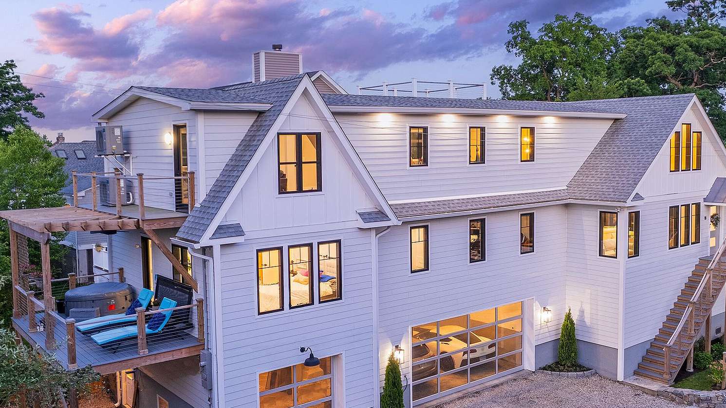 Twilight exterior of a Mike and Kim listing at 18 Channel Avenue in Norwalk, a lit white modern cape under a pink cloud sky