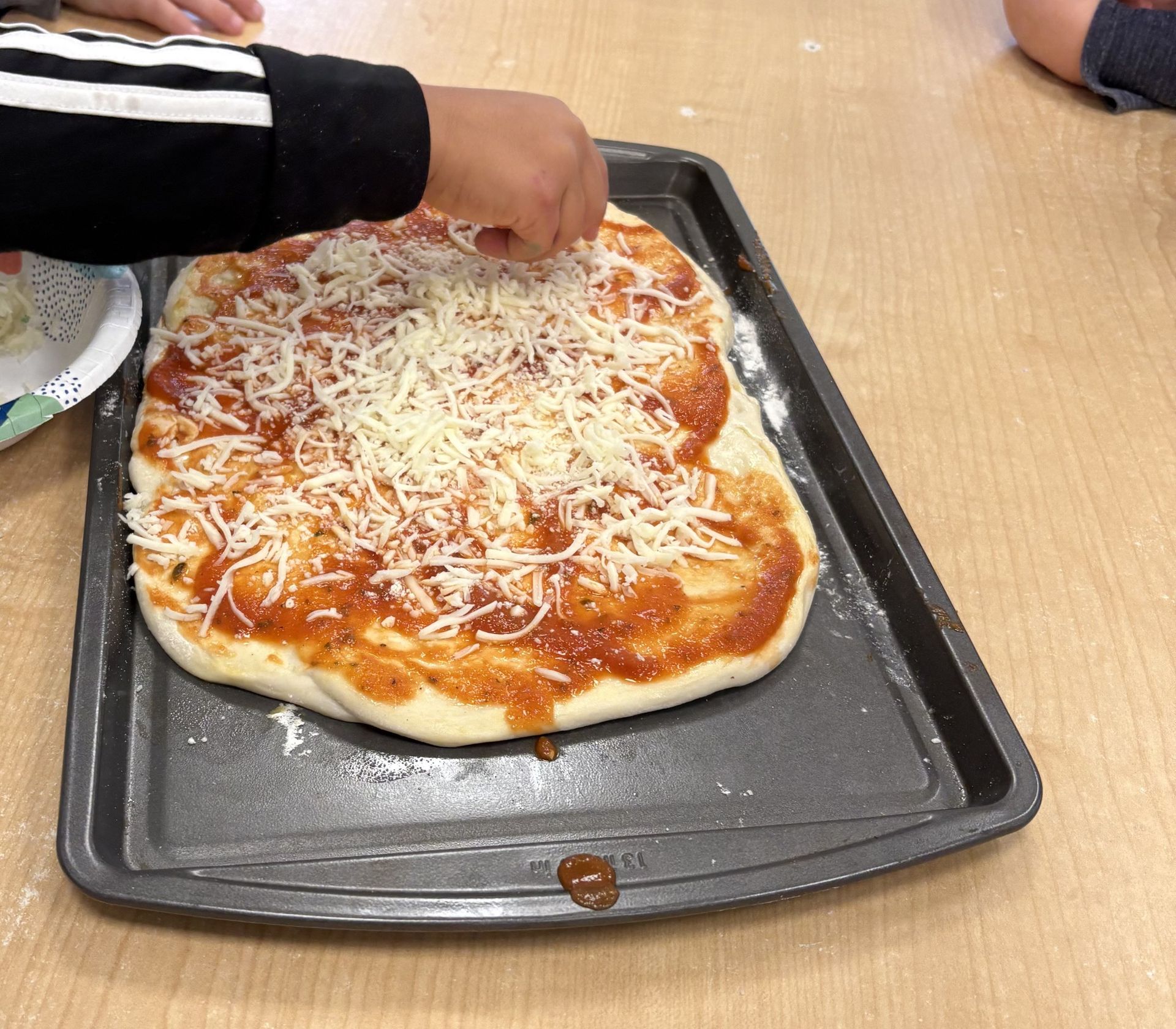 A student sprinkling cheese over a homemade pizza