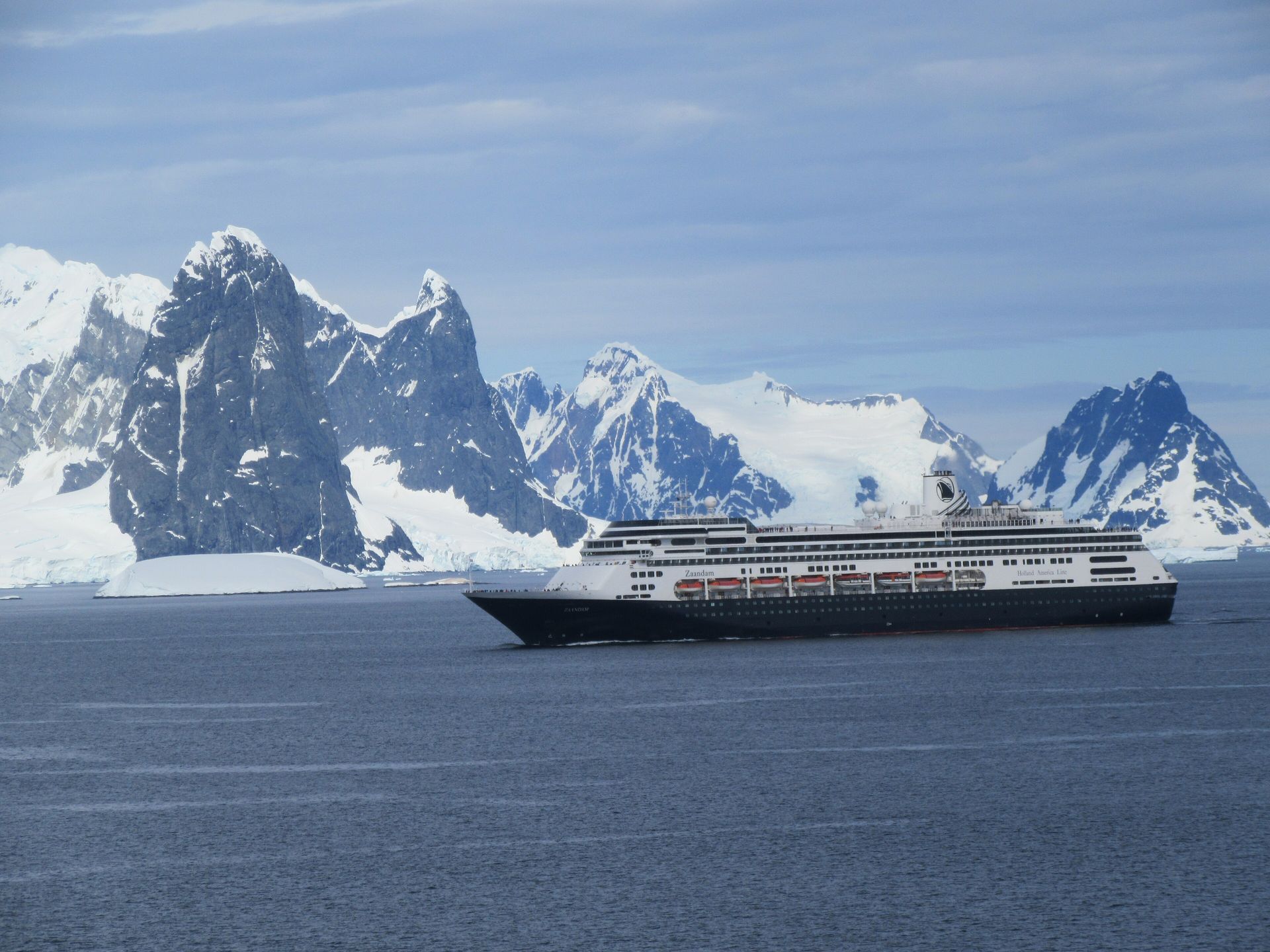 Holland America's Zaandam, a large cruise ship with a dark blue hull, sailing past snow-covered peaks in the Neumaier Channel, Antarctica