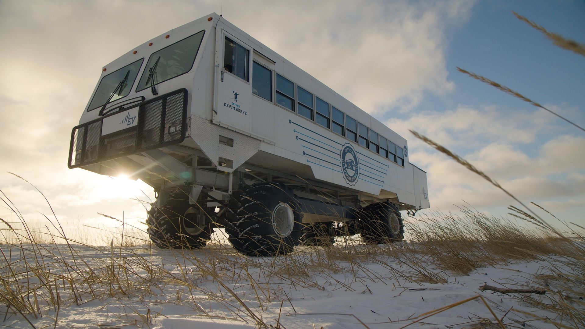An electric Tundra Buggy on large tires stands on snowy tundra grass near Churchill, Manitoba