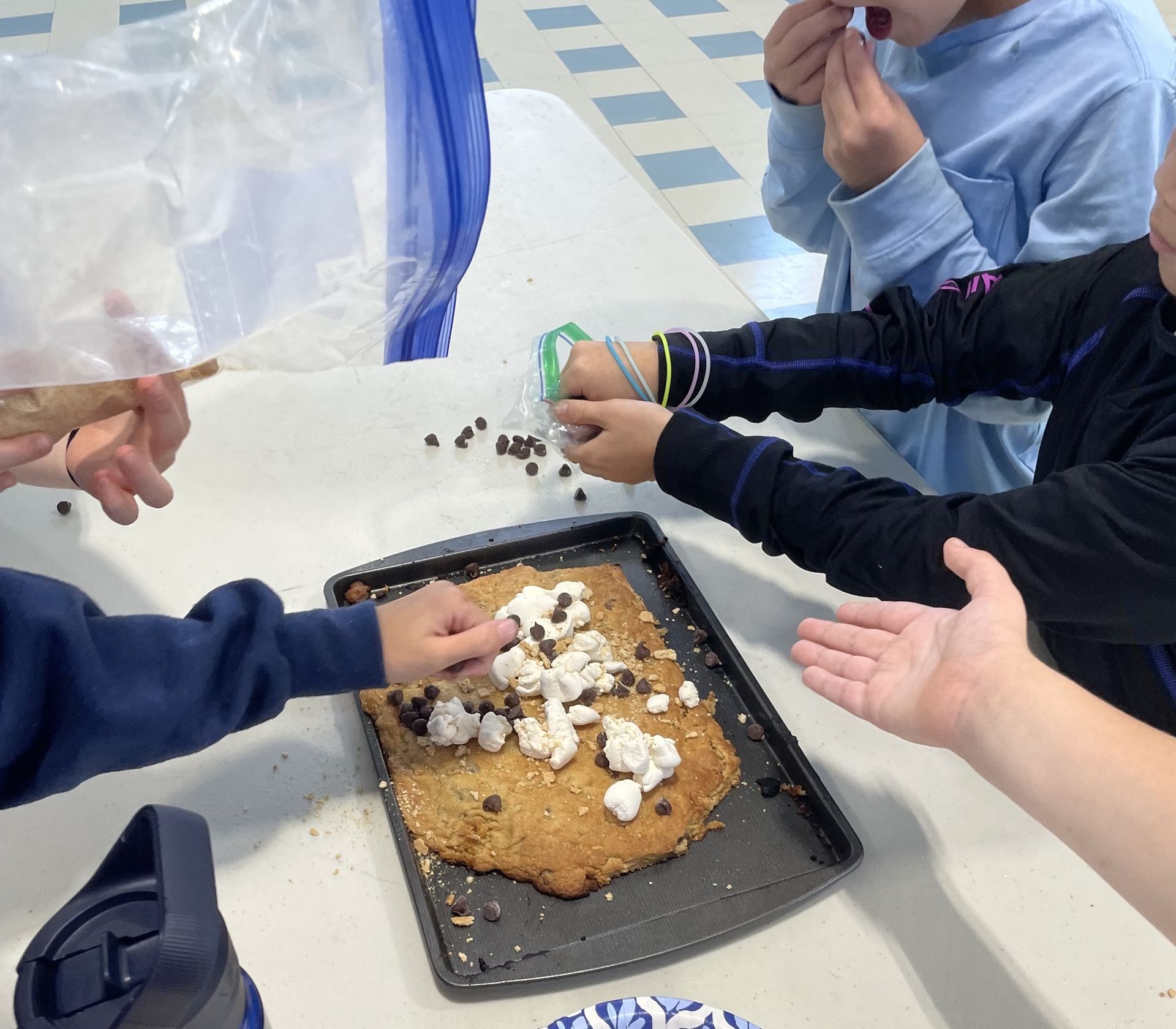 Students topping a giant cookie with marshmallows and chocolate chips together