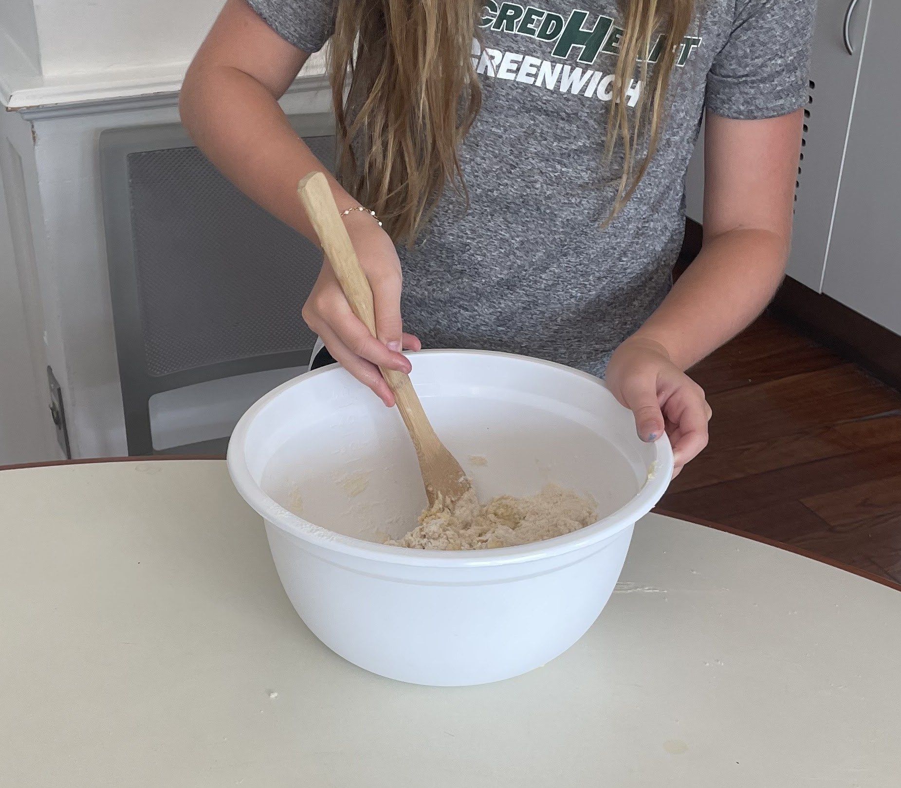 A Sacred Heart Greenwich student mixing dough with a wooden spoon