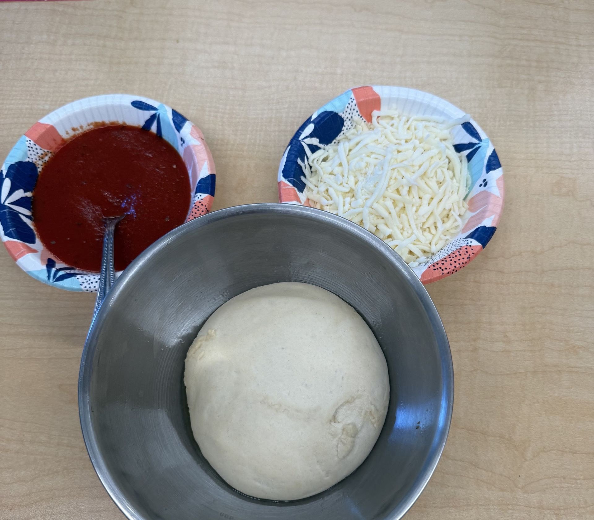 Pizza dough with bowls of sauce and cheese ready for summer campers