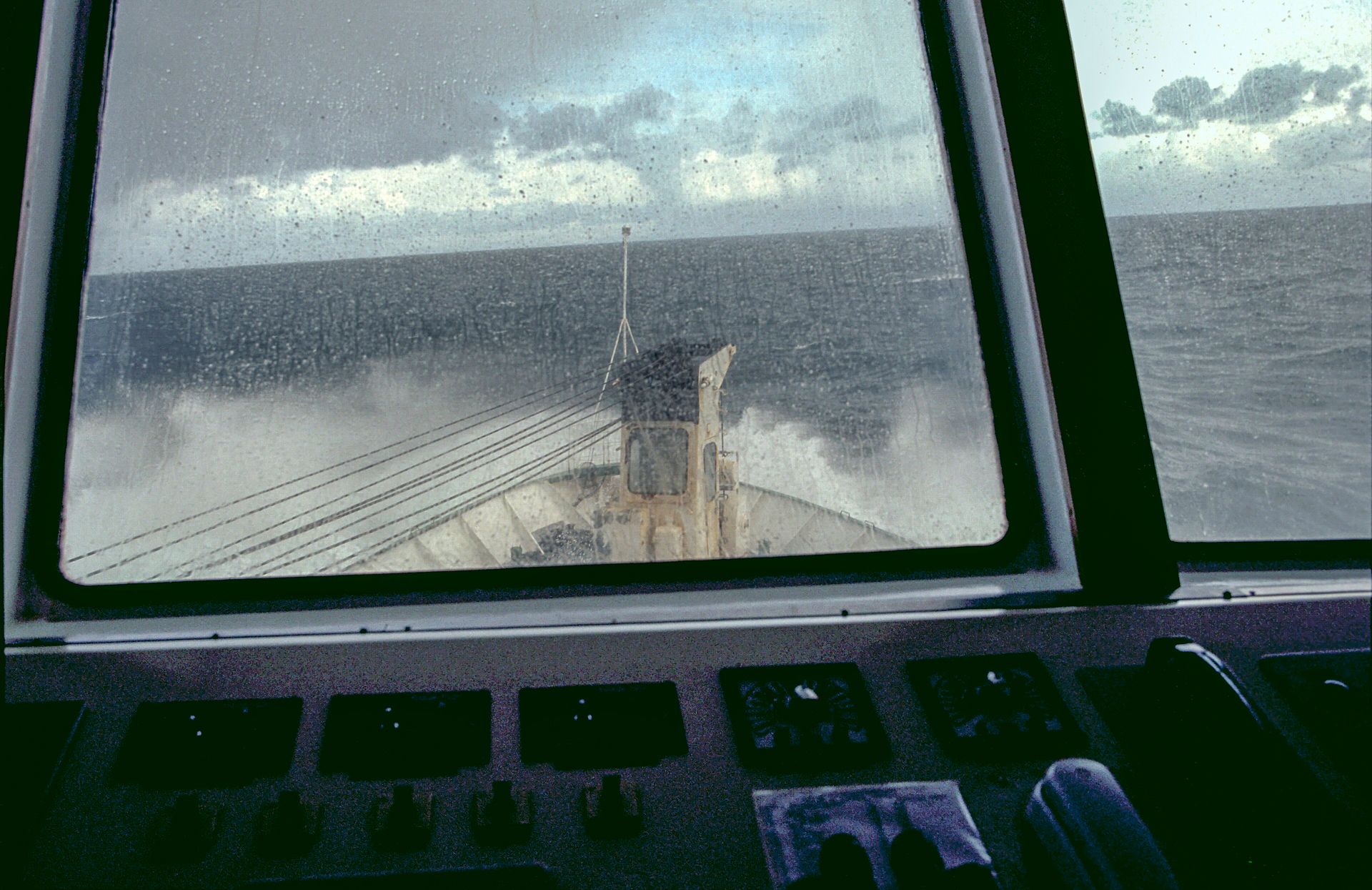 Spray breaking over a ship's bow in gray, choppy seas, seen through the bridge windows in the Drake Passage