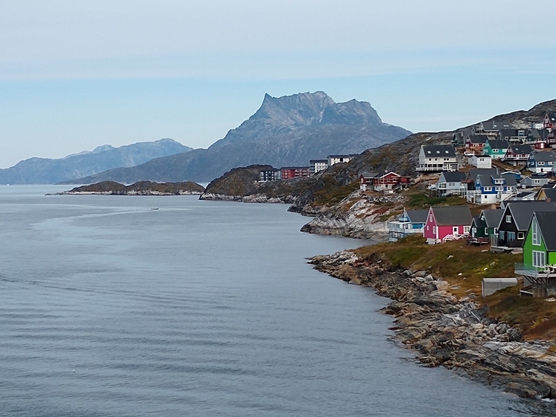 Colorful houses on a rocky shore in Nuuk, Greenland, with a jagged mountain across the fjord