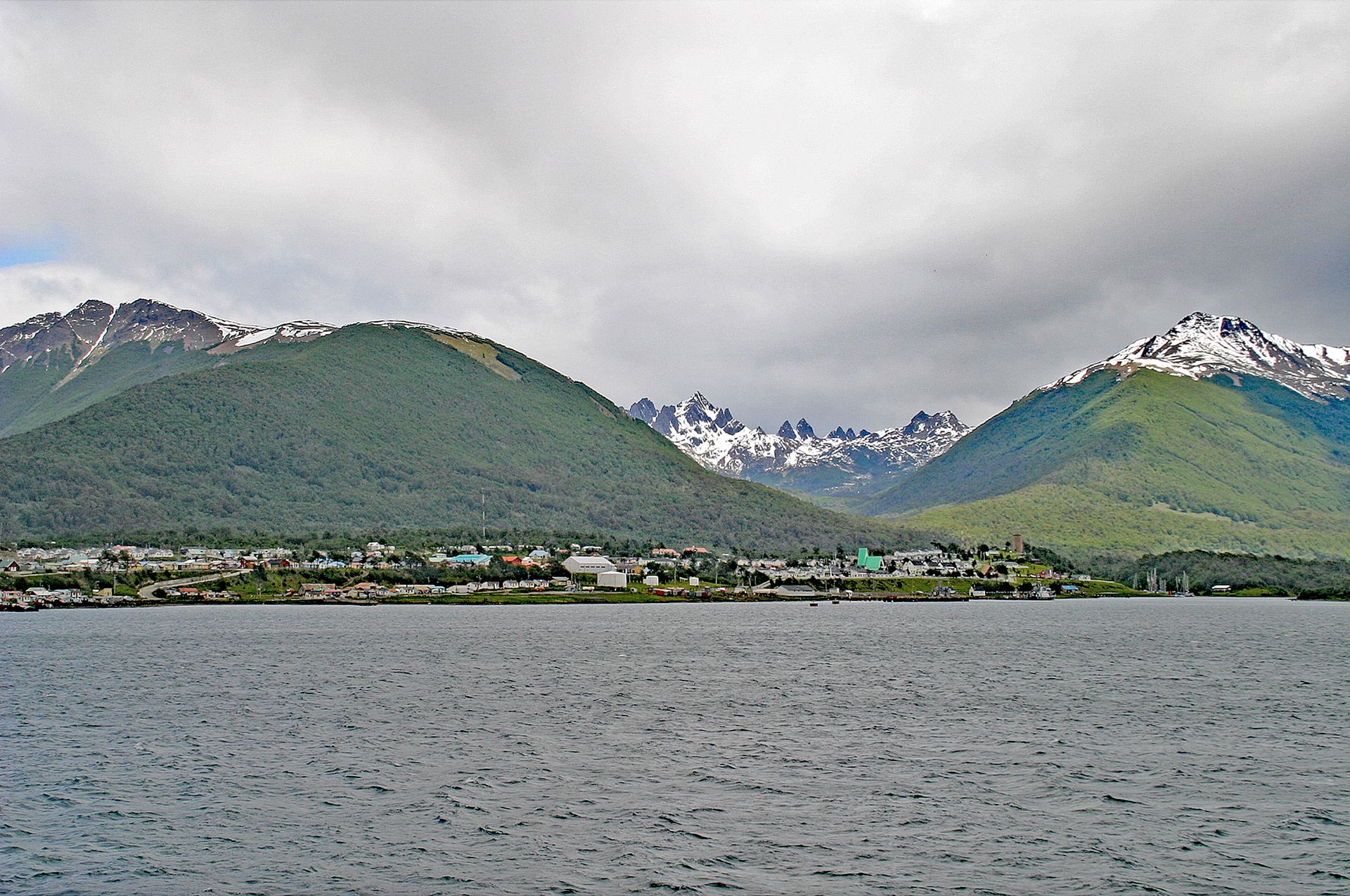 Puerto Williams on the shore of the Beagle Channel, with forested hills and snow-capped peaks rising behind the town