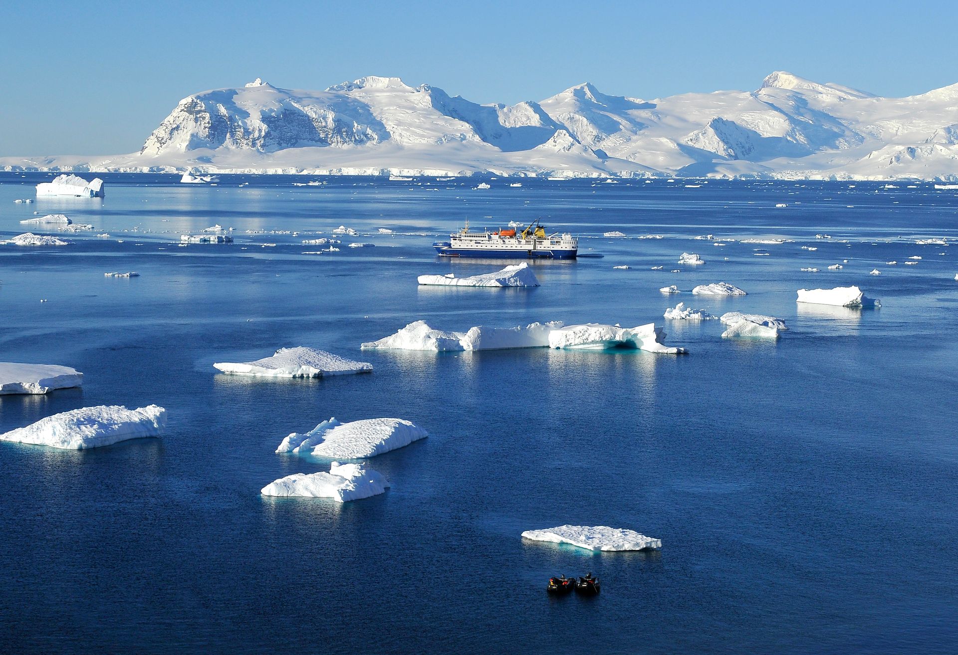 An expedition cruise ship and two Zodiacs among floating ice in the Errera Channel, with snow-covered mountains behind
