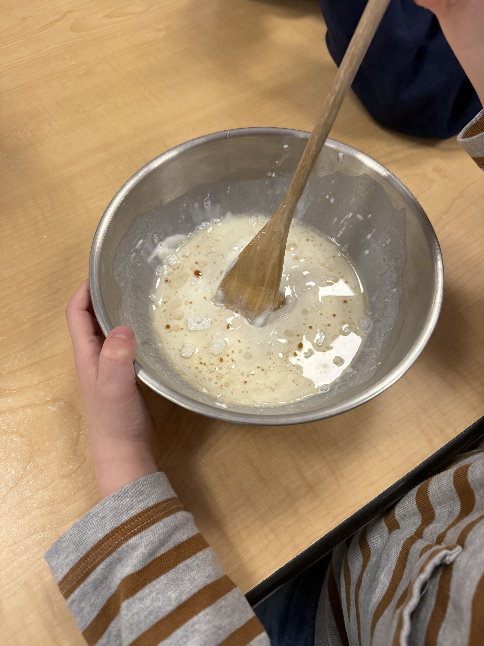 A child stirring milk, egg, and vanilla with a wooden spoon