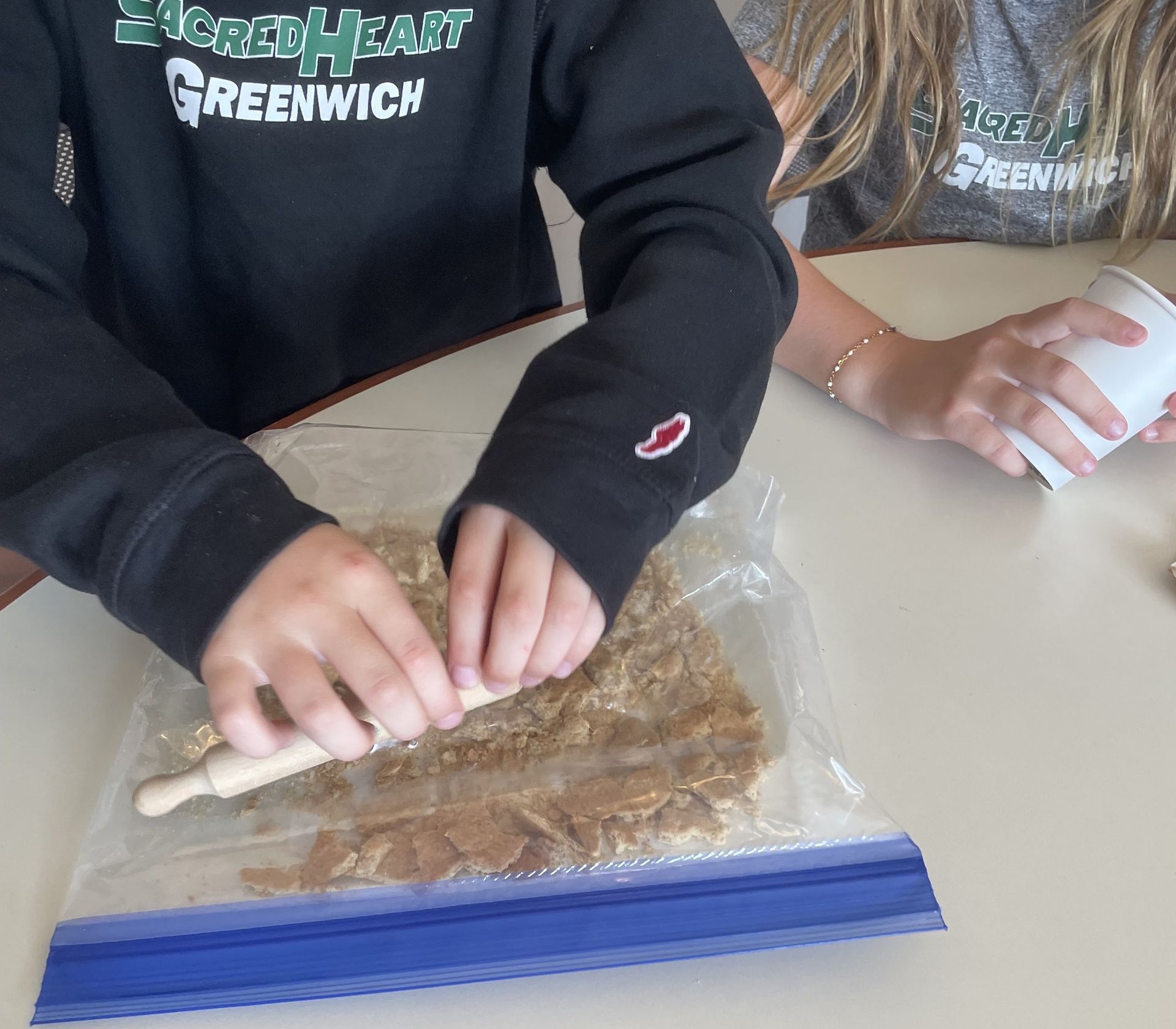 A student crushing cookies in a bag with a rolling pin