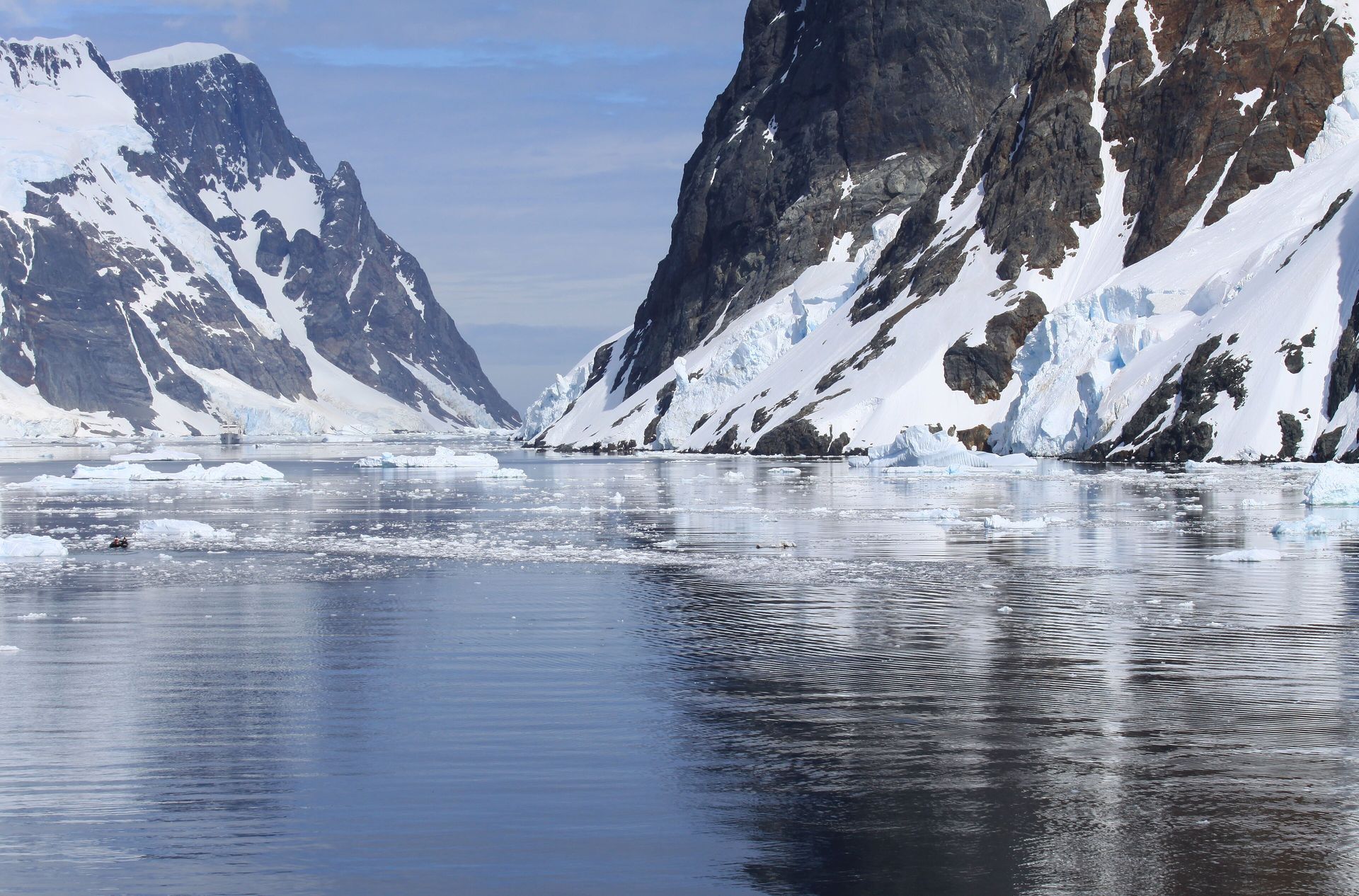 The narrow entrance of the Lemaire Channel between steep snow-covered cliffs, with brash ice on the water