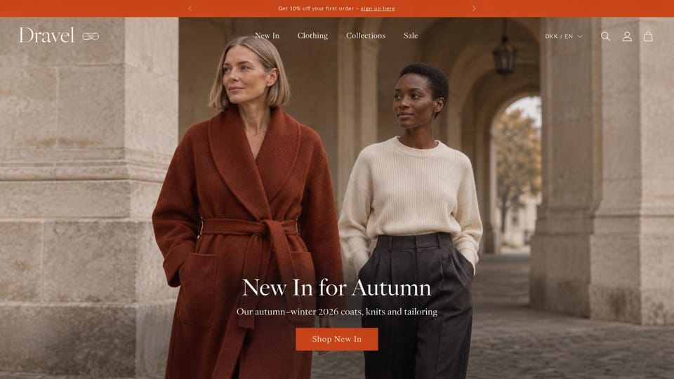 Fashion website design, autumn coats and knits under a stone arcade: orange top bar, a white serif logo with a knot mark, two women walking under a stone arcade in a rust belted wool coat and a cream sweater with charcoal trousers, a centered white serif headline and an orange button