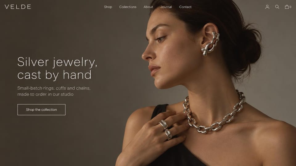 Jewelry website design, cast silver jewelry on warm taupe: taupe background, a woman in profile wearing a chunky silver chain, a molten silver ear cuff and two rings, thin white sans wordmark and headline, outlined white shop button