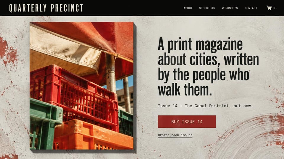 News and magazine website design, city print quarterly with a textured background: black top bar with a cream condensed wordmark, plaster textured background with rust red marks, a cover photo of stacked red, green and orange market crates, condensed black headline, red buy button