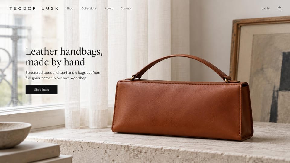 Fashion website design, handmade leather handbags in a still life: a cognac structured top-handle bag on a stone ledge by sheer curtains and an abstract framed painting, a serif headline and a black button