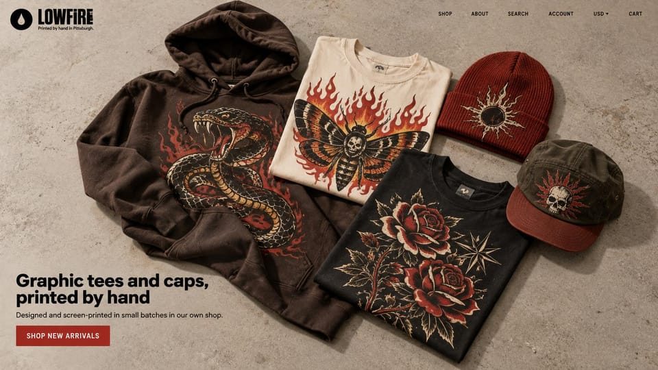Fashion website design, screen-printed streetwear in a flat lay: concrete surface with a brown snake-print hoodie, a cream moth tee, a black rose tee, a red sun beanie and an olive skull cap, a bold black logo, a black sans headline and a red button