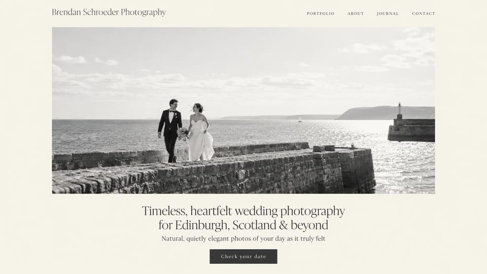 Wedding photographer website design, coastal wedding photographer with one framed black and white photo: ivory page, a small serif name, a wide black-and-white photo of a couple walking along a stone harbor wall, a centered dark serif headline and a dark button