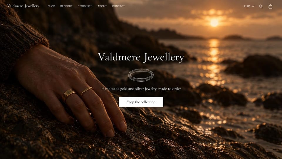 Jewelry website design, made-to-order rings on a rocky shore at sunset: dark full-screen photo of a hand in gold rings resting on wet rocks at sunset, white serif name centered over a drawn ring, white shop button, thin white menu