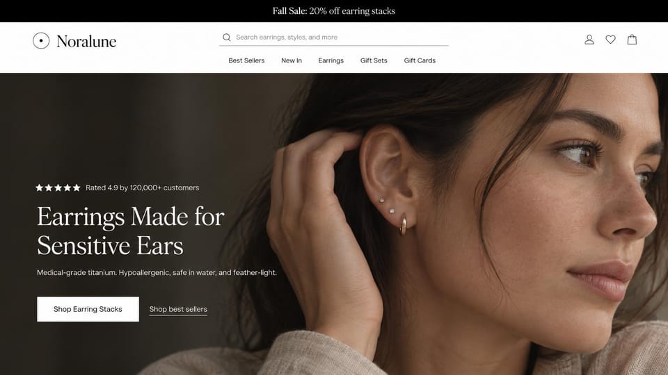 Jewelry website design, earrings for sensitive ears with a review line: black sale bar, white menu with a search bar, a dark-haired woman touching her ear stacked with small gold studs, a white serif headline and a white button
