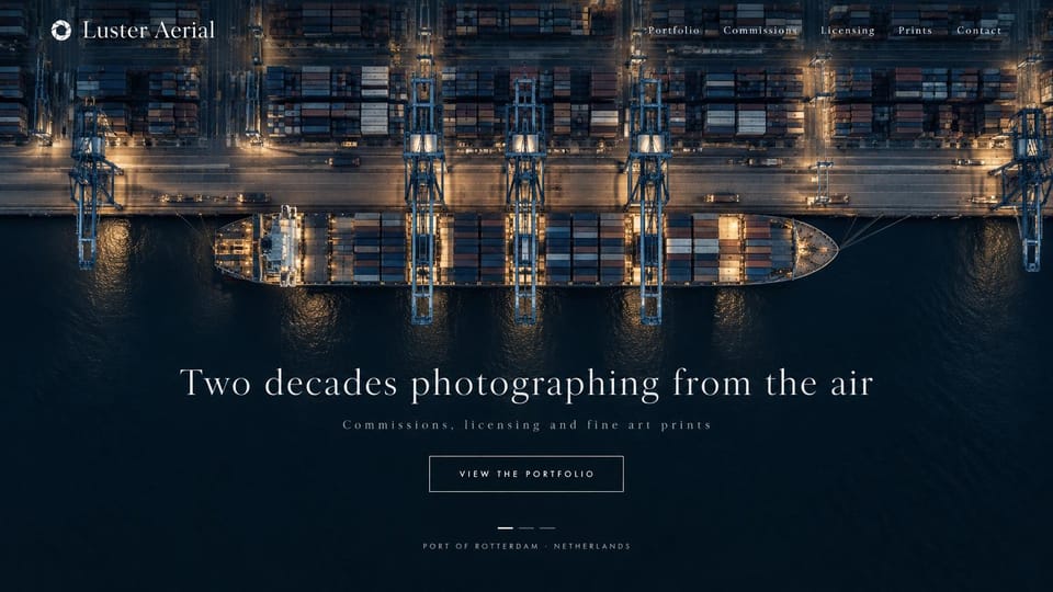 Photography website design, aerial photography from above: a night aerial photo of a container port in navy and amber, a centered serif headline and an outlined button
