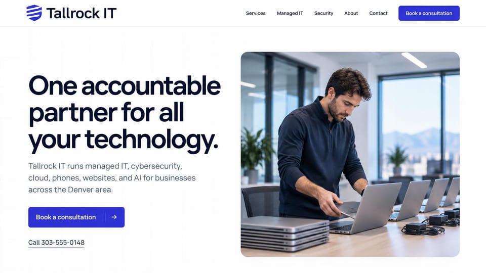 IT company website design, managed IT with a laptop rollout: white page, oversized navy headline, blue consultation button, a technician setting up a row of laptops in a bright office