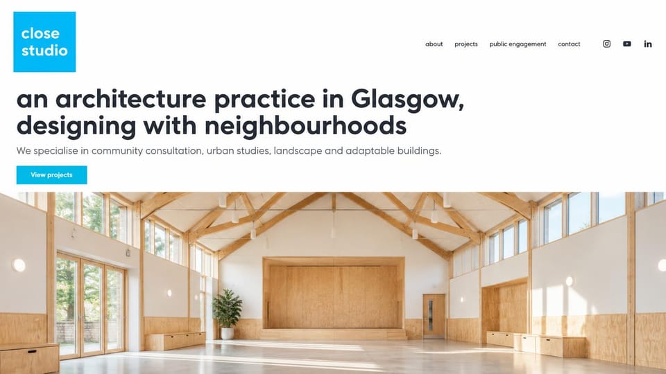 Architecture website design, community architecture with a plain lowercase headline: white page, a bright blue square logo and button, a large bold lowercase headline, a wide photo of a sunlit timber community hall