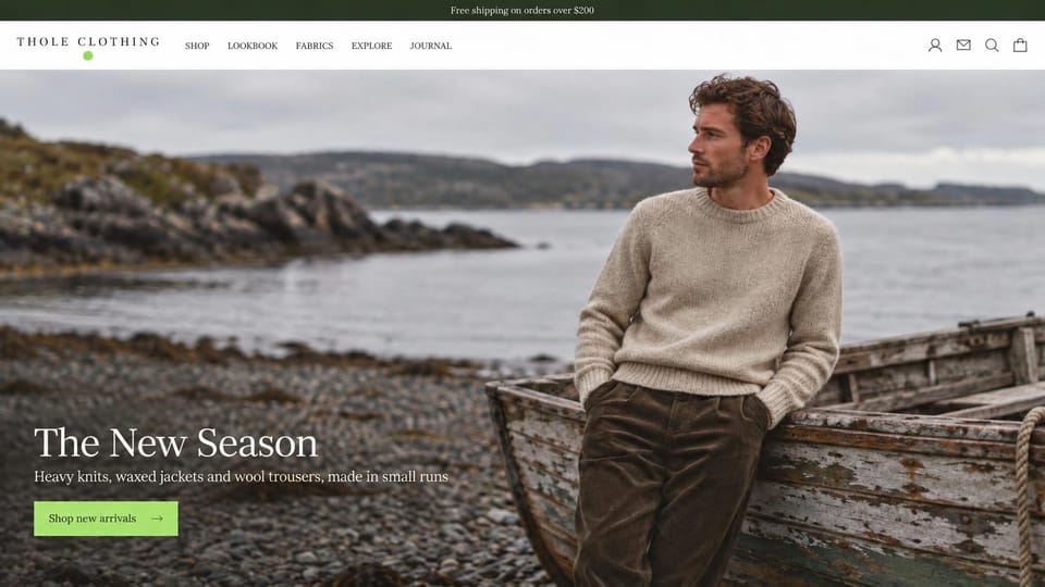 Fashion website design, knits and waxed jackets by an old rowboat: dark green top bar, a man in an oatmeal sweater leaning on a weathered rowboat on a pebble beach, a white serif headline and a lime button
