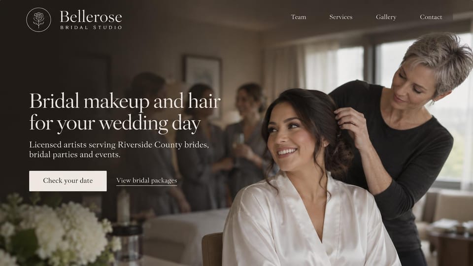 Makeup artist website design, licensed bridal studio in warm, dim light: dim warm photo of a gray-haired stylist arranging a smiling bride's hair while bridesmaids chat behind, a white serif headline, a cream date button and a packages link