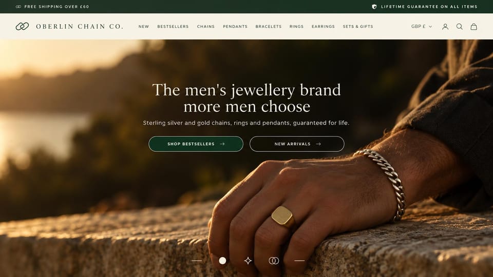Jewelry website design, men's chains and signet rings at golden hour: dark green top bar, cream menu, a man's hand on stone at sunset wearing a silver chain bracelet and gold signet, a centered white serif headline and two outlined buttons