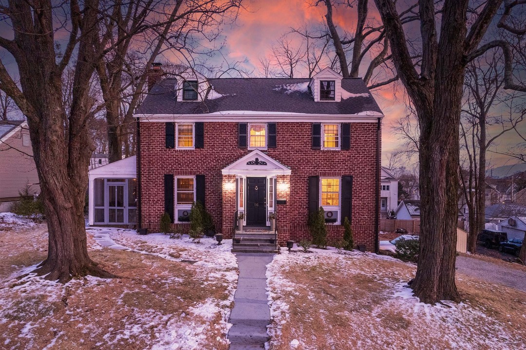 Twilight listing photo of a red brick colonial with fresh snow under a salmon sunset sky