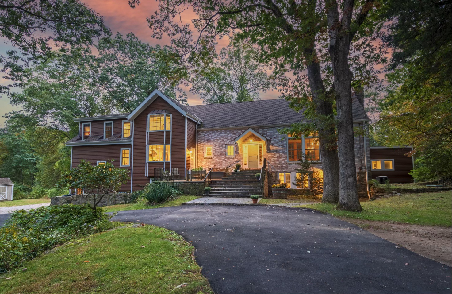 Twilight listing photo of a stone-front colonial with every window lit under a pink dusk sky