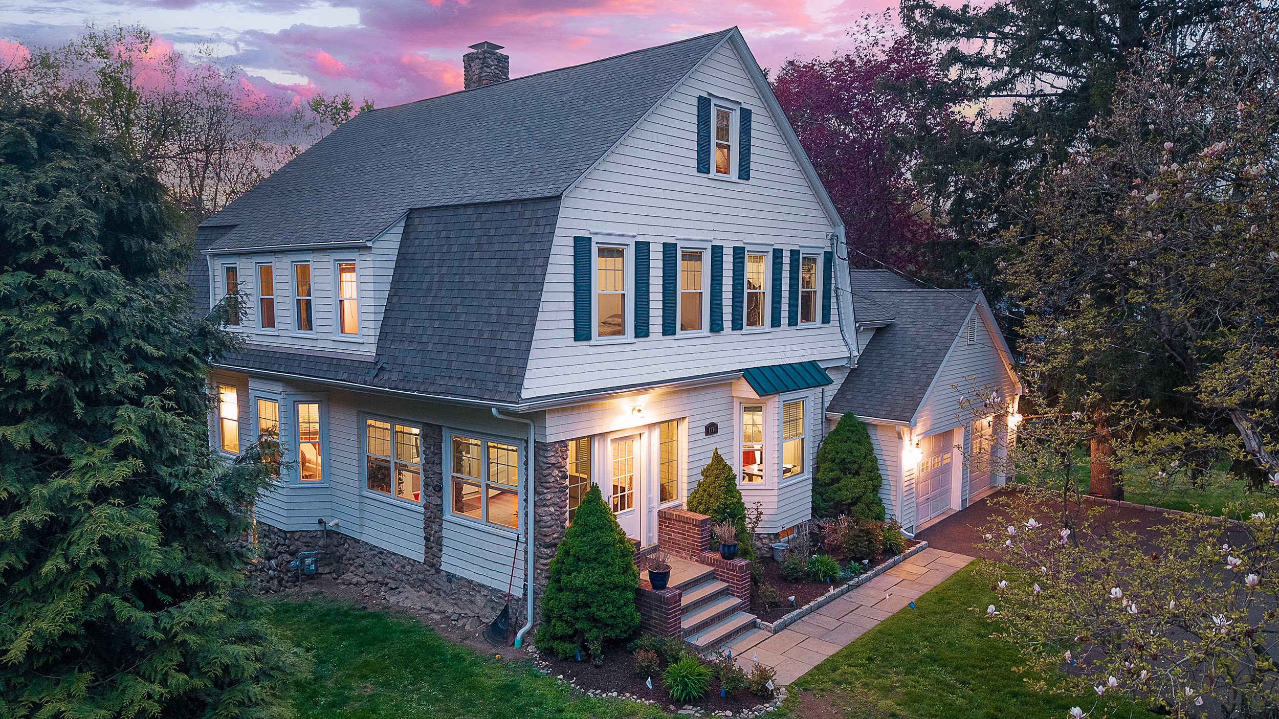 Twilight listing photo of a gambrel colonial with blue shutters under a pink evening sky